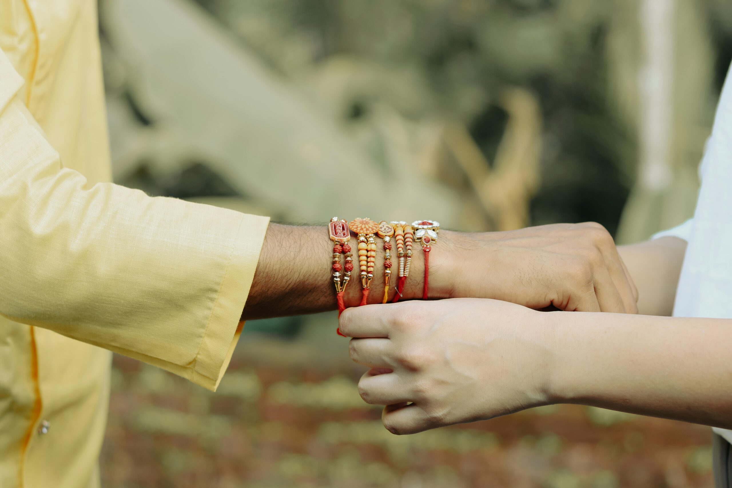 Close-up of hands tying a Rakhi bracelet, symbolizing sibling bond in traditional Indian culture.